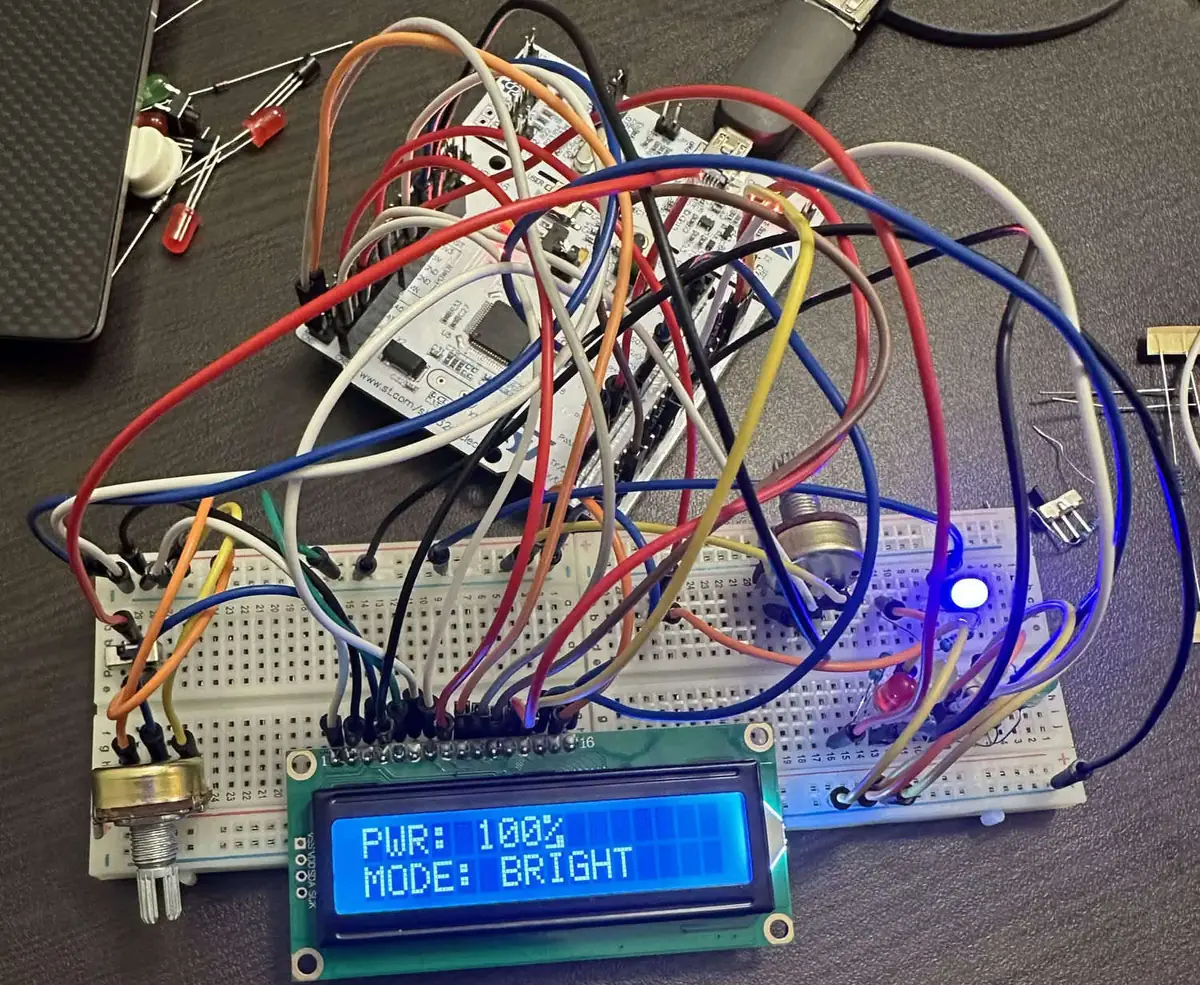 Breadboard build: an STM32 Nucleo board wired to a 16x2 LCD reading PWR: 100% and MODE: BRIGHT, with a potentiometer and LEDs